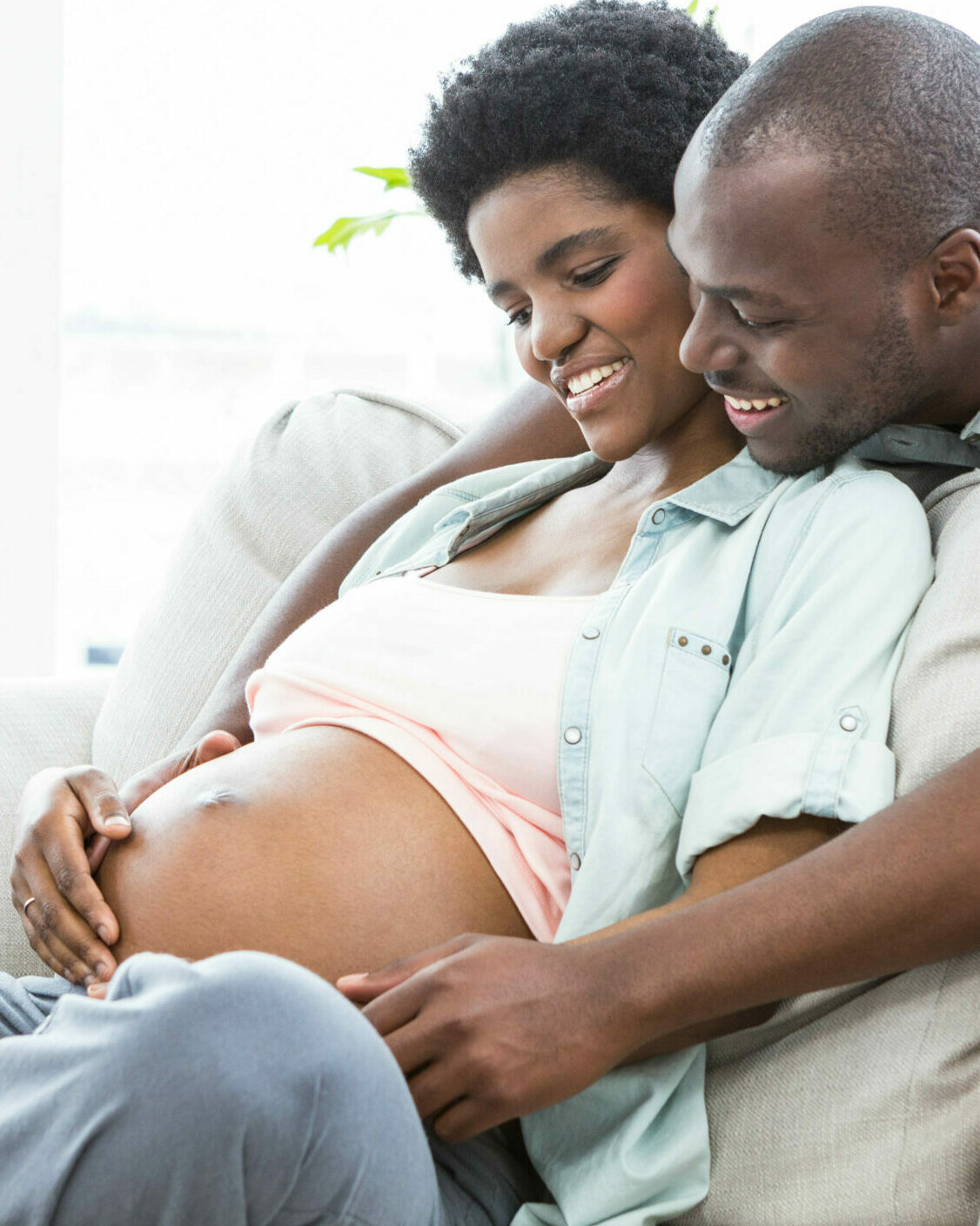 Man touching pregnant womans stomach on sofa at home